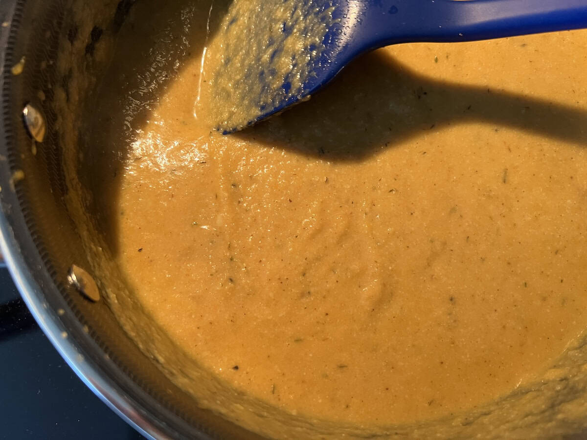 a smooth and velvety pumpkin cauliflower soup in a soup pot, being stirring with a blue spatula.