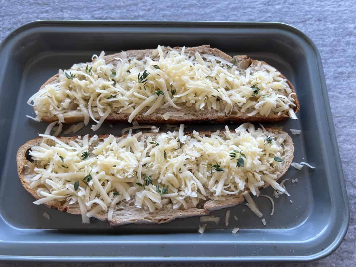 shredded cheese and fresh thyme are sprinkled on two oblong slices of bread. 
