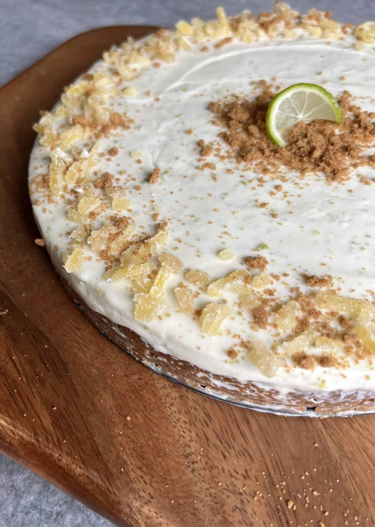 key lime cheesecake on a wooden serving board. the close up angle shows the thick graham cracker crust under a layer of silky cheesecake filling.