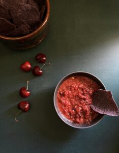 cherry salsa in a bowl with a blue corn tortilla chip dunked halfway into it.