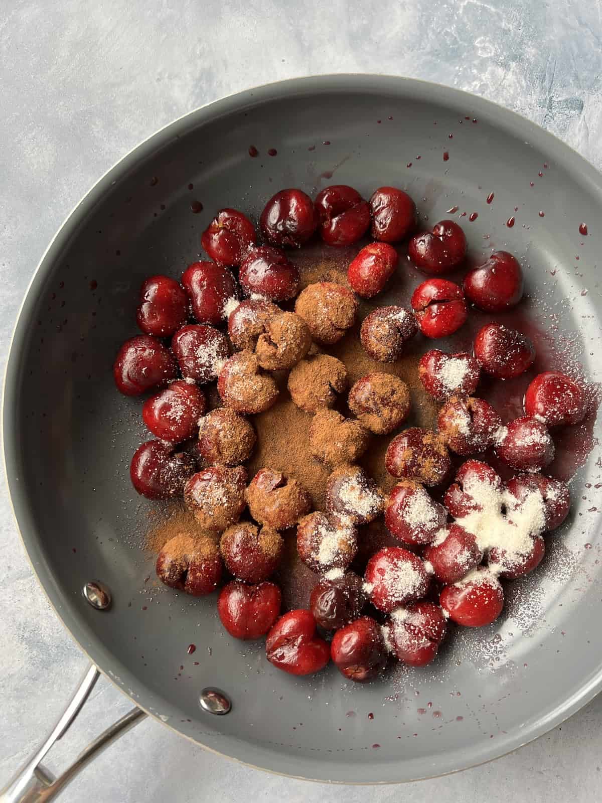 a mixture of fresh cherries, sugar, cinnamon, lemon juice, salt, and water in a wide skillet with a gray nonstick coating. 