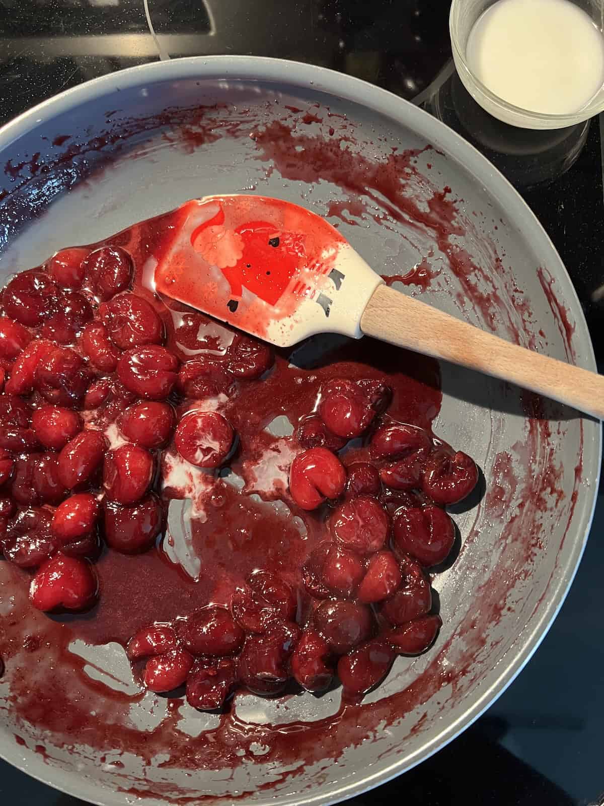 white colored cornstarch slurry is added to the pan with the cherry mixture, contrasting against the red coloring of the sauce. 