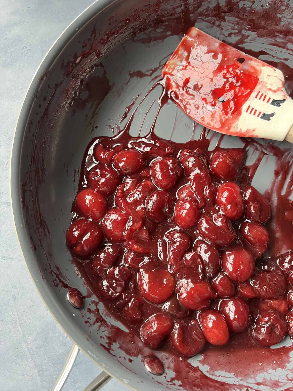 the finished cherry compote in the skillet, bearing a deep red color, glossy texture, and thick consistency. 
