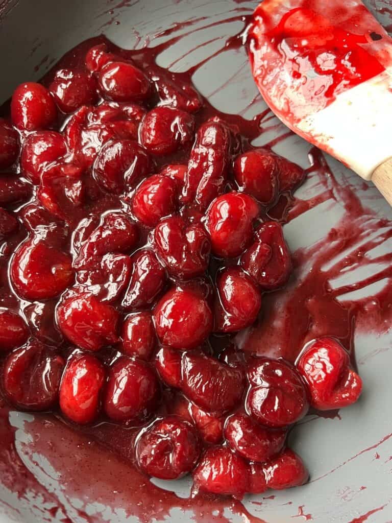 a close up of thick and glossy red cherry compote cooking in a skillet