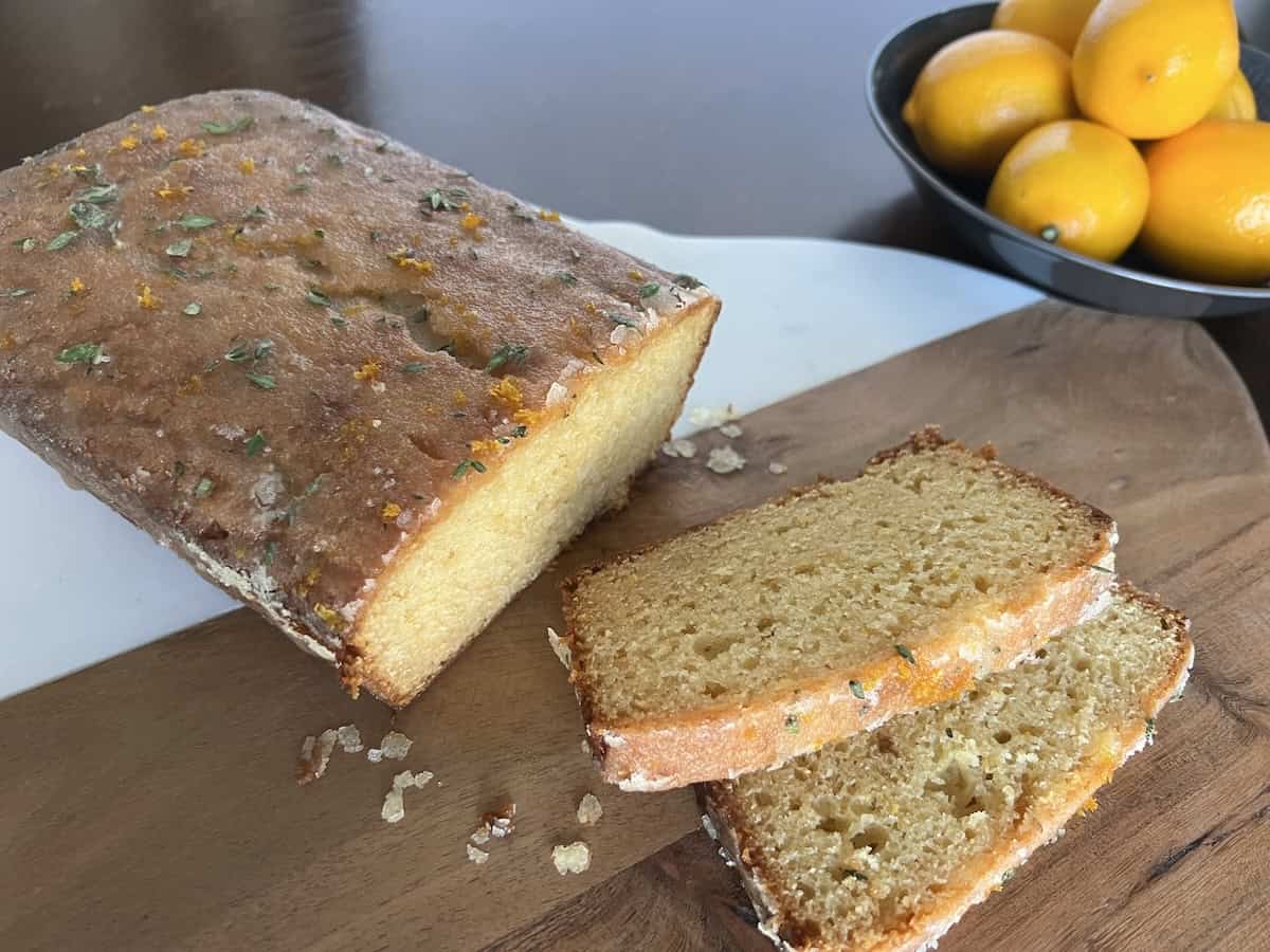 sliced meyer lemon cake on a two-tone cutting board, next to a bowl of brightly colored meyer lemons.
