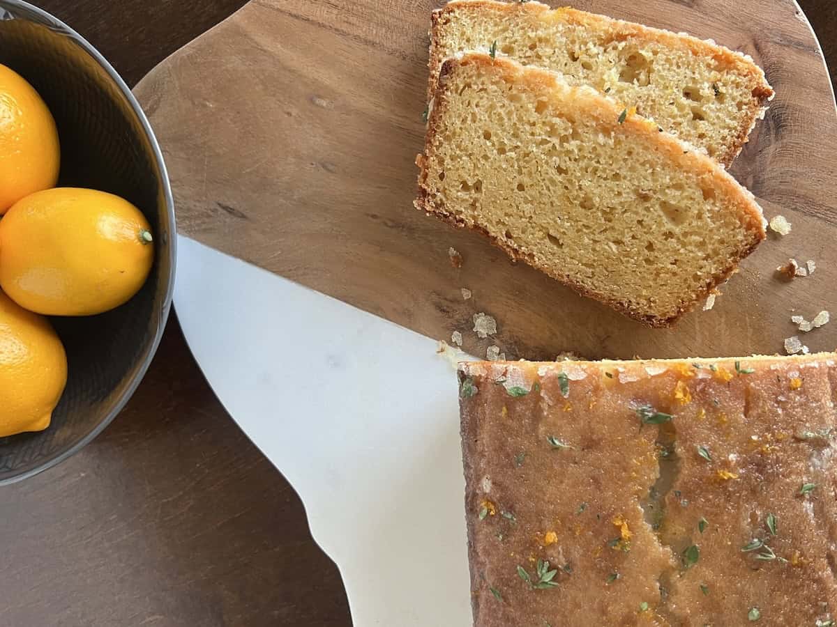 sliced meyer lemon cake on a two-tone cutting board, next to a bowl of brightly colored meyer lemons.