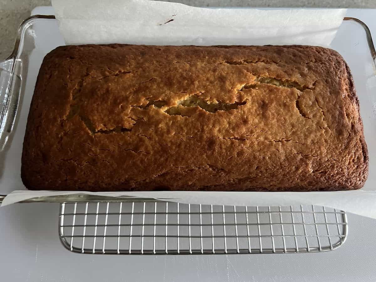 the parchment paper lined load pan from step one, with a baked meyer lemon pound cake inside it. there are a few cracks in the surface of the cake and it has deep golden browning around the edges.