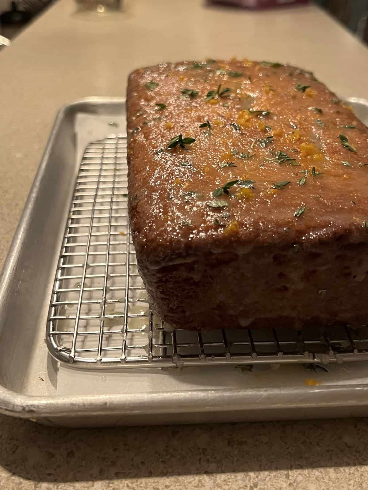 the fully glazed meyer lemon cake sitting on a metal wire rack on a baking sheet. the surface of the cake is shiny and wet-looking.