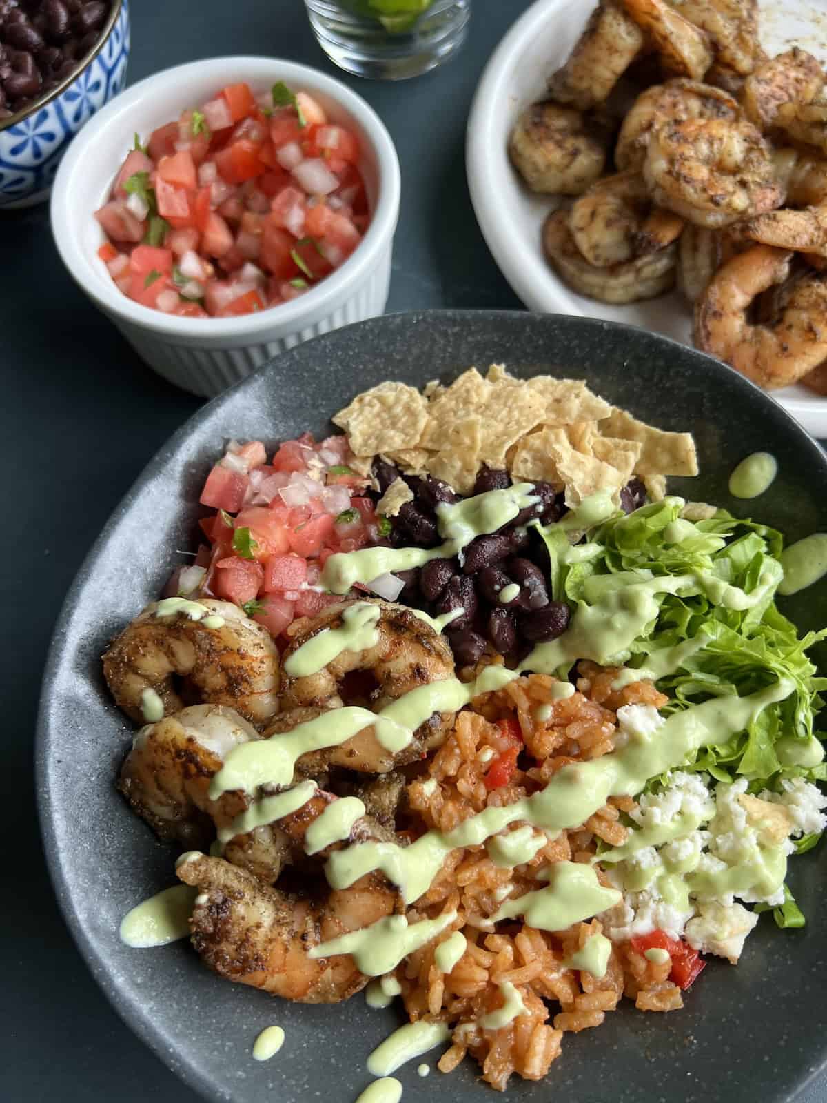 a finished shrimp burrito bowl, mounded high with shrimp, black beans, and toppings while avocado crema has been drizzled across in diagonal lines.