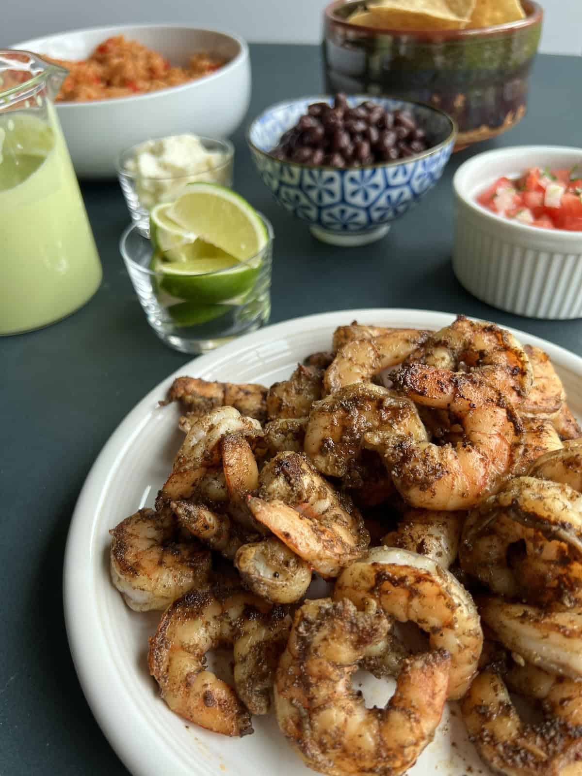 all of the components for the shrimp burrito bowls arranged on the countertop, with the cooked shrimp front and center, flanked by black beans, cooked Spanish rice, the avocado crema, and various other toppings.