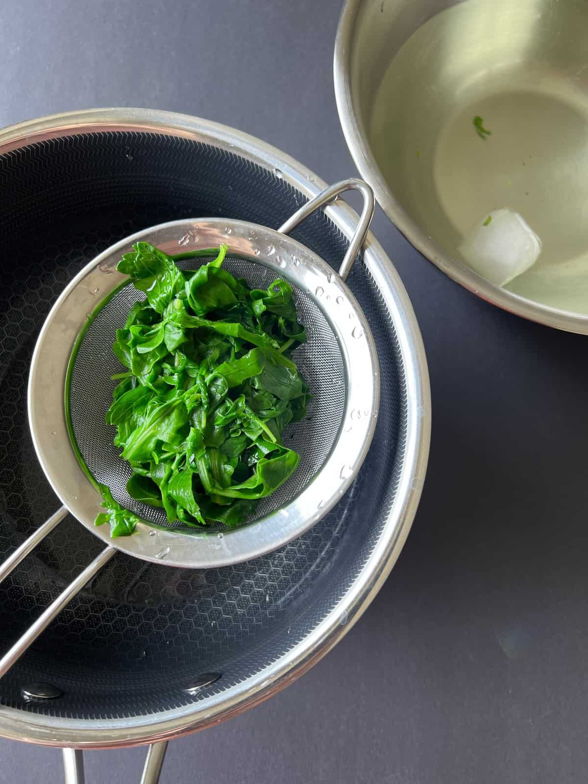 the greens are placed in the strainer set over the pot and drained of excess water.