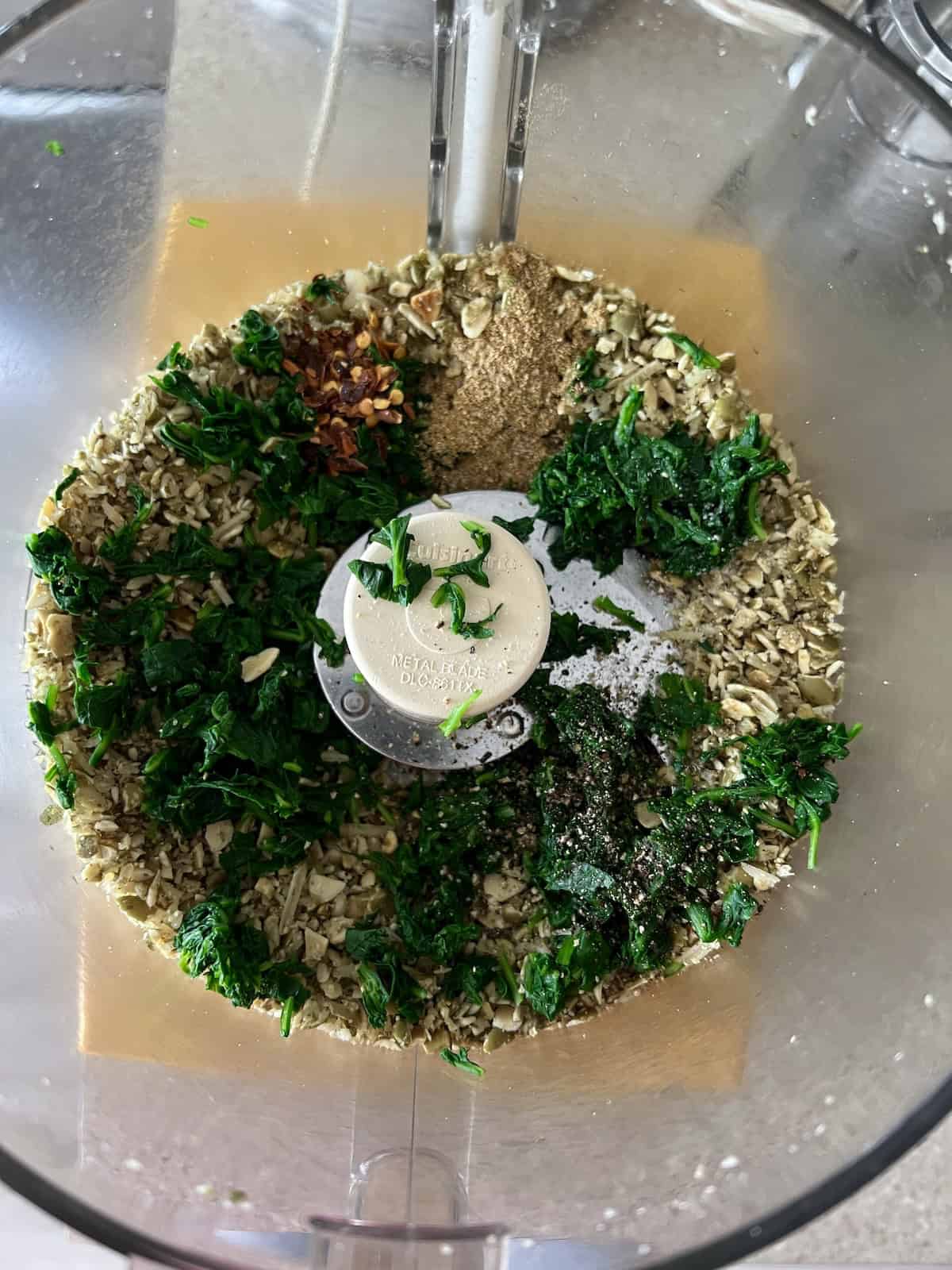 greens and seasonings are added to the pumpkin seed mixture in the food processor
