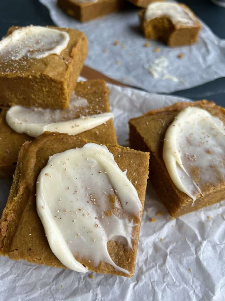 cream cheese frosted pumpkin spice blondies are stacked on sheets of parchment paper and sprinkled with fresh nutmeg