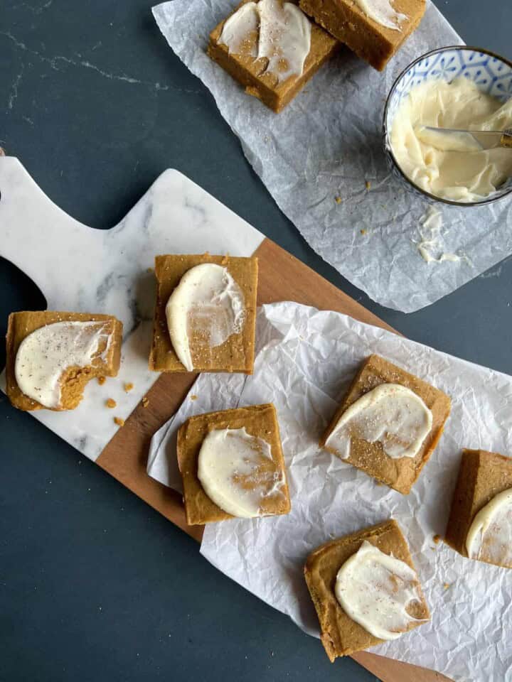pumpkin spice blondies are frosted with a swoop of cream cheese frosting and arranged on a cutting board