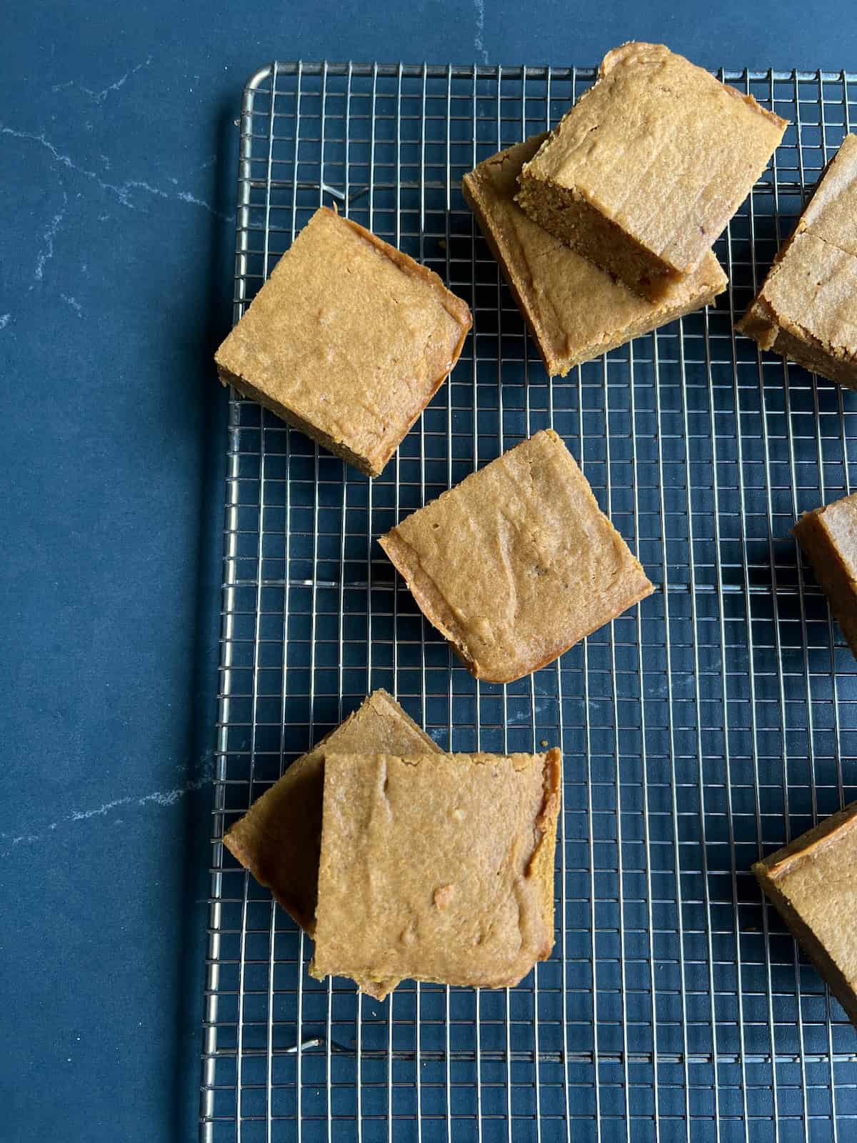 the block of blondies is sliced into smaller squares and arranged on the cooling rack.