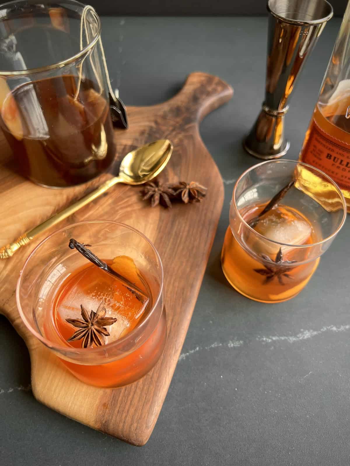 two vanilla chai old fashioned cocktails are served in rocks glasses and garnished with a strip of vanilla bean and whole star anise.