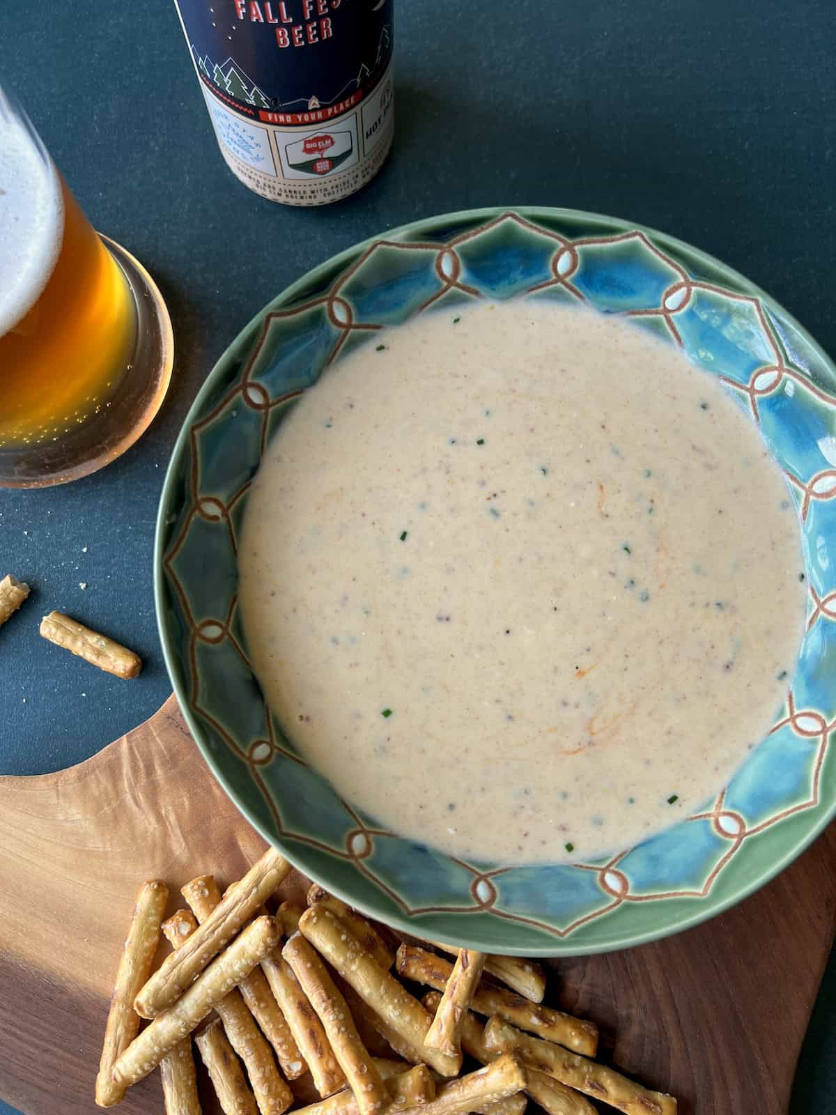 a wide bowl of oktoberfest beer cheese on a rustic wooden surface next to a mug of beer and can it was poured from