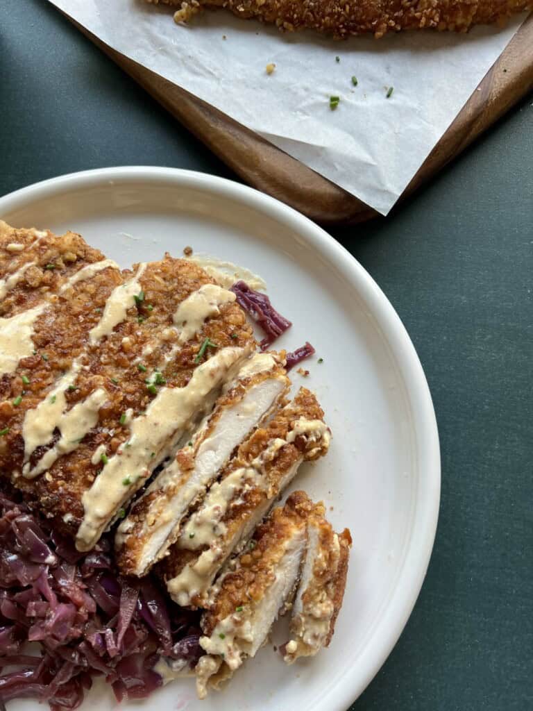 a sliced piece of pretzel crusted chicken schnitzel is served on a bed of sauteed red cabbage and drizzled with Oktoberfest beer cheese