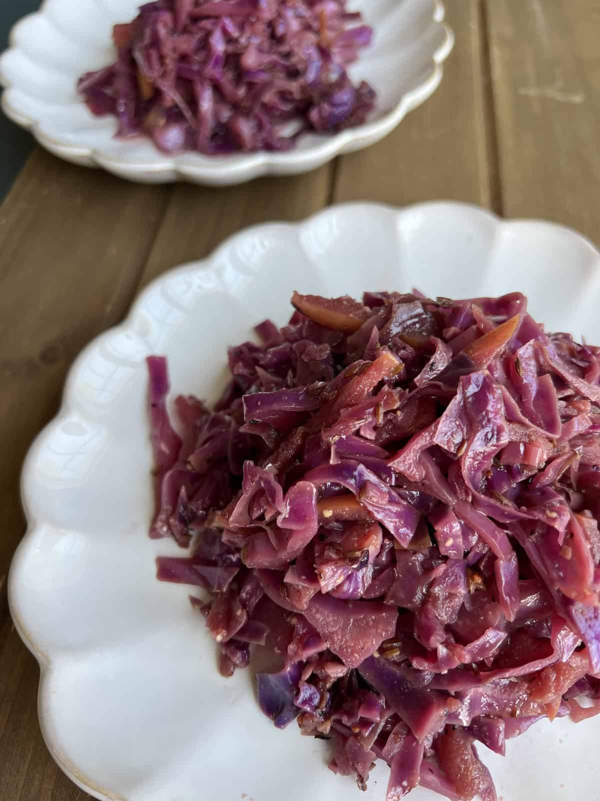 two plates of sauteed red cabbage served on a rustic wooden table.