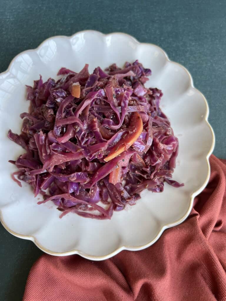 sauteed red cabbage is piled on a fluted plate, with visible apple slices and mustard seeds.