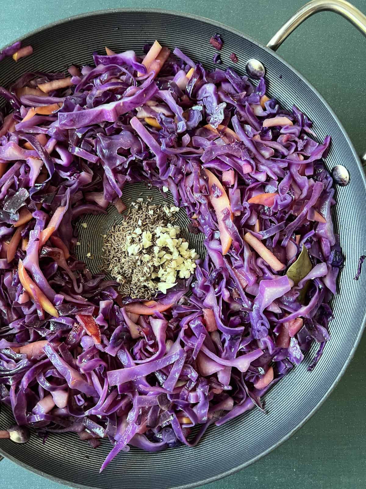 the cabbage mixture is pushed to the sides of the skillet, creating a well in the center where garlic and caraway seeds are added.