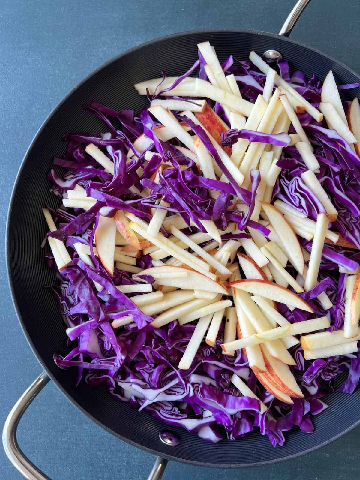 a wide skillet containing sliced red cabbage and apple slices
