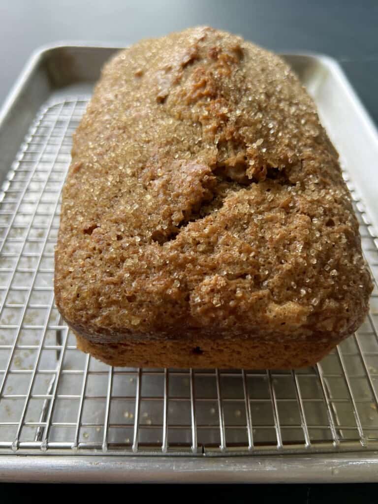 a loaf of acorn squash bread has a domed top and is resting on a wire rack lined baking sheet