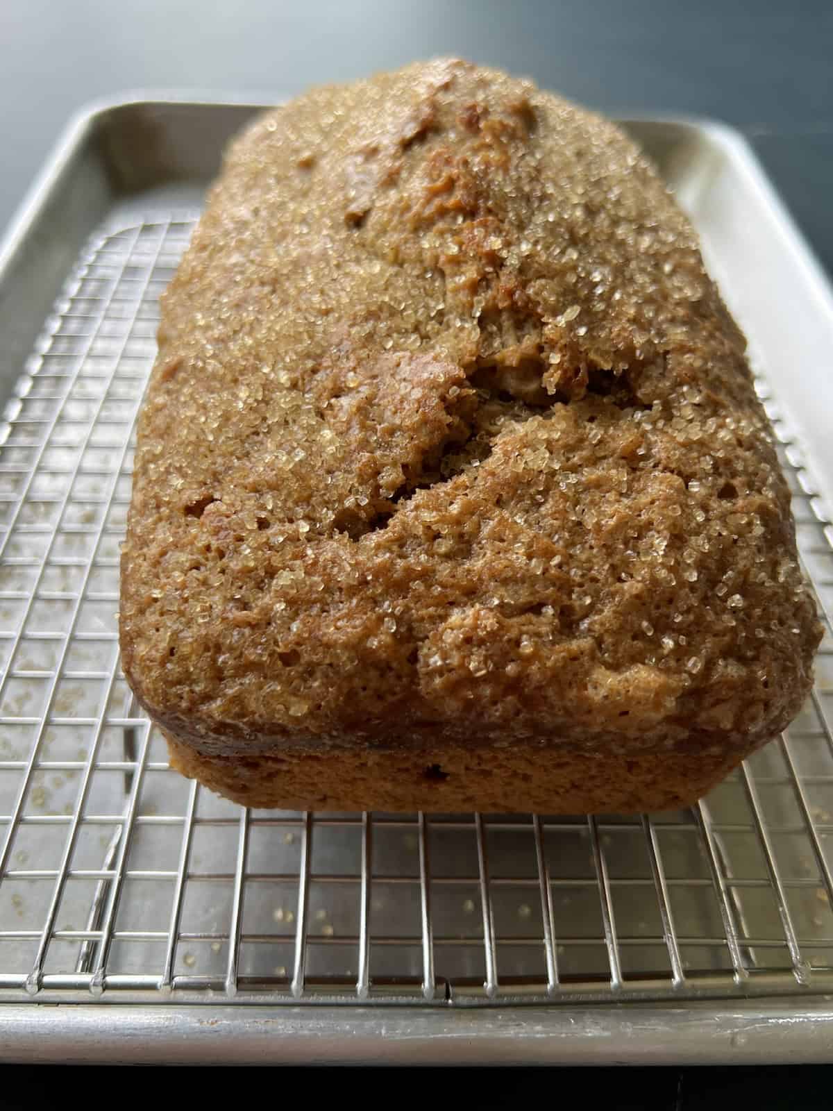 a loaf of acorn squash bread has a domed top and is resting on a wire rack lined baking sheet