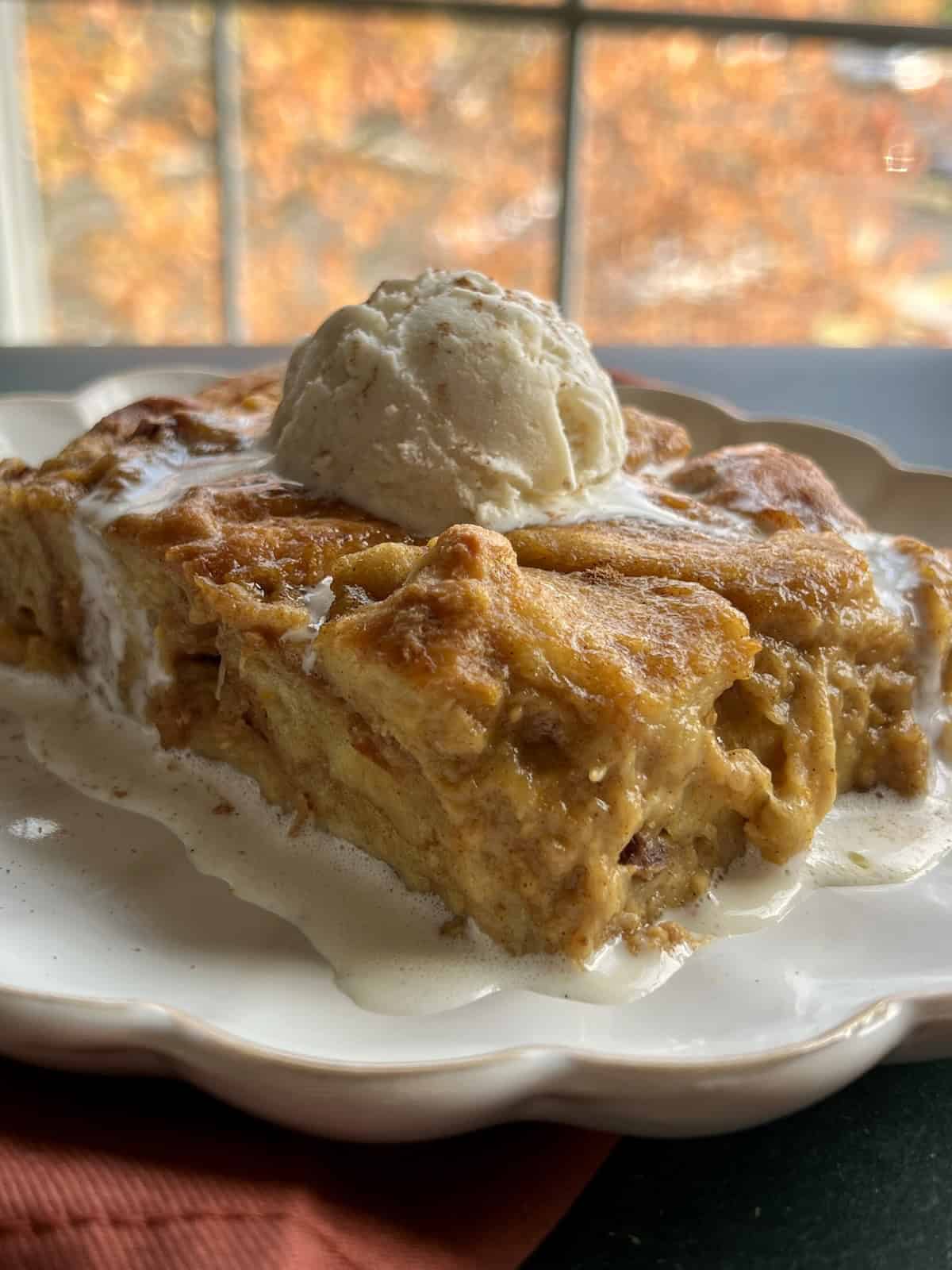 a scoop of vanilla ice cream slowly melts atop a slice of pumpkin brioche bread pudding