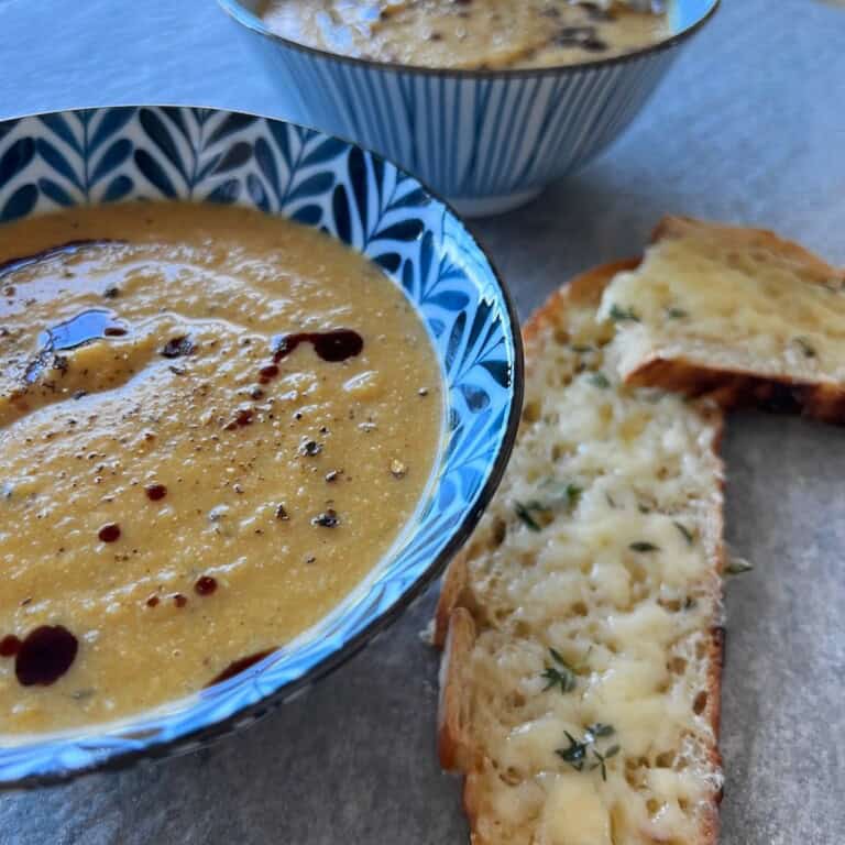 2 bowls of creamy pumpkin cauliflower soup on a table, served with cheesy thyme toast