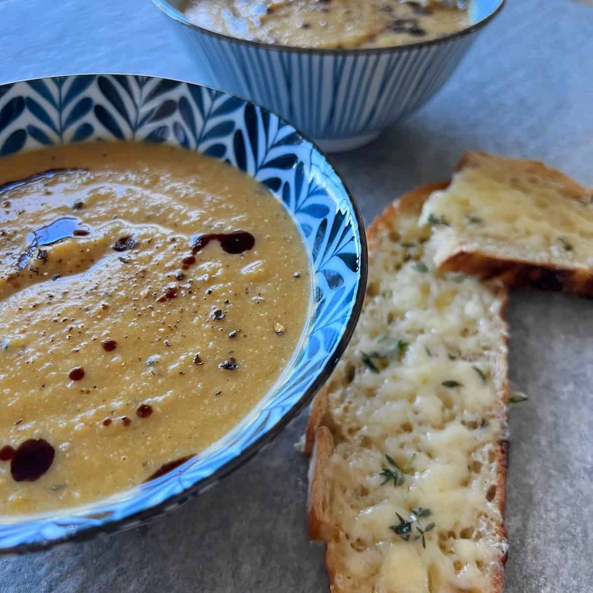 2 bowls of creamy pumpkin cauliflower soup on a table, served with cheesy thyme toast