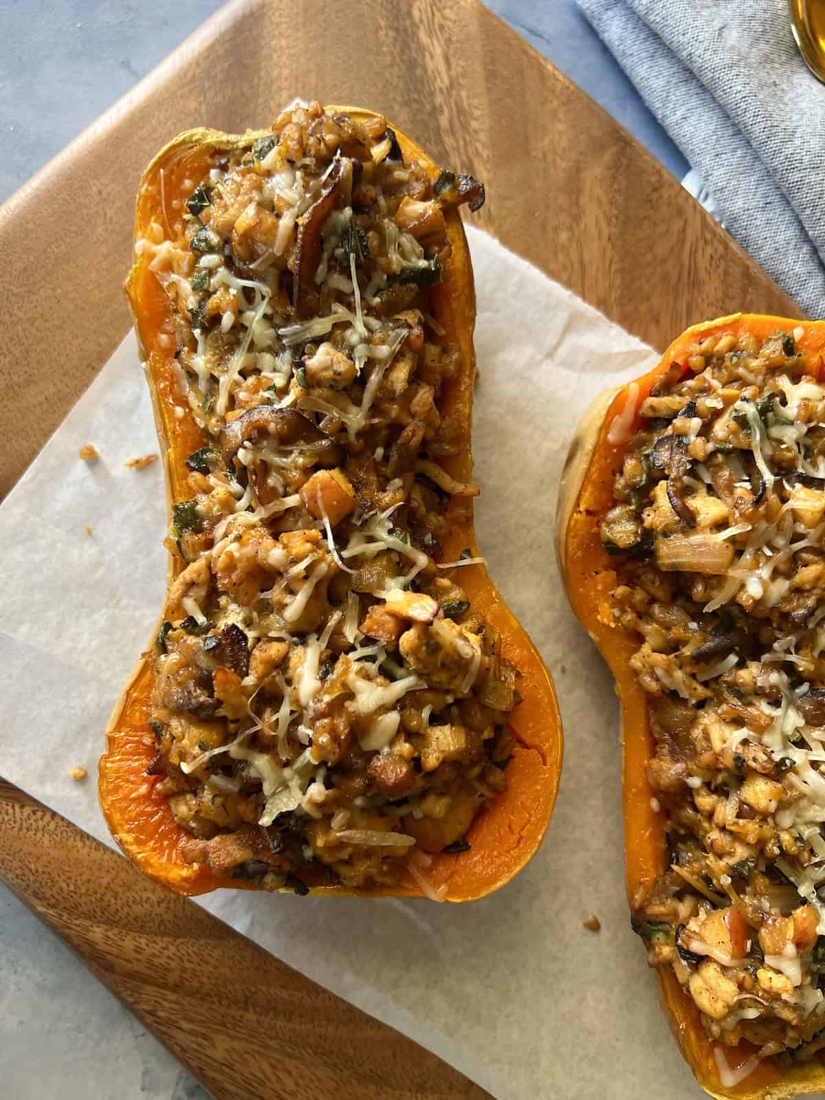 two stuffed butternut squash halves are topped with melted parmesan cheese and served on a wooden board