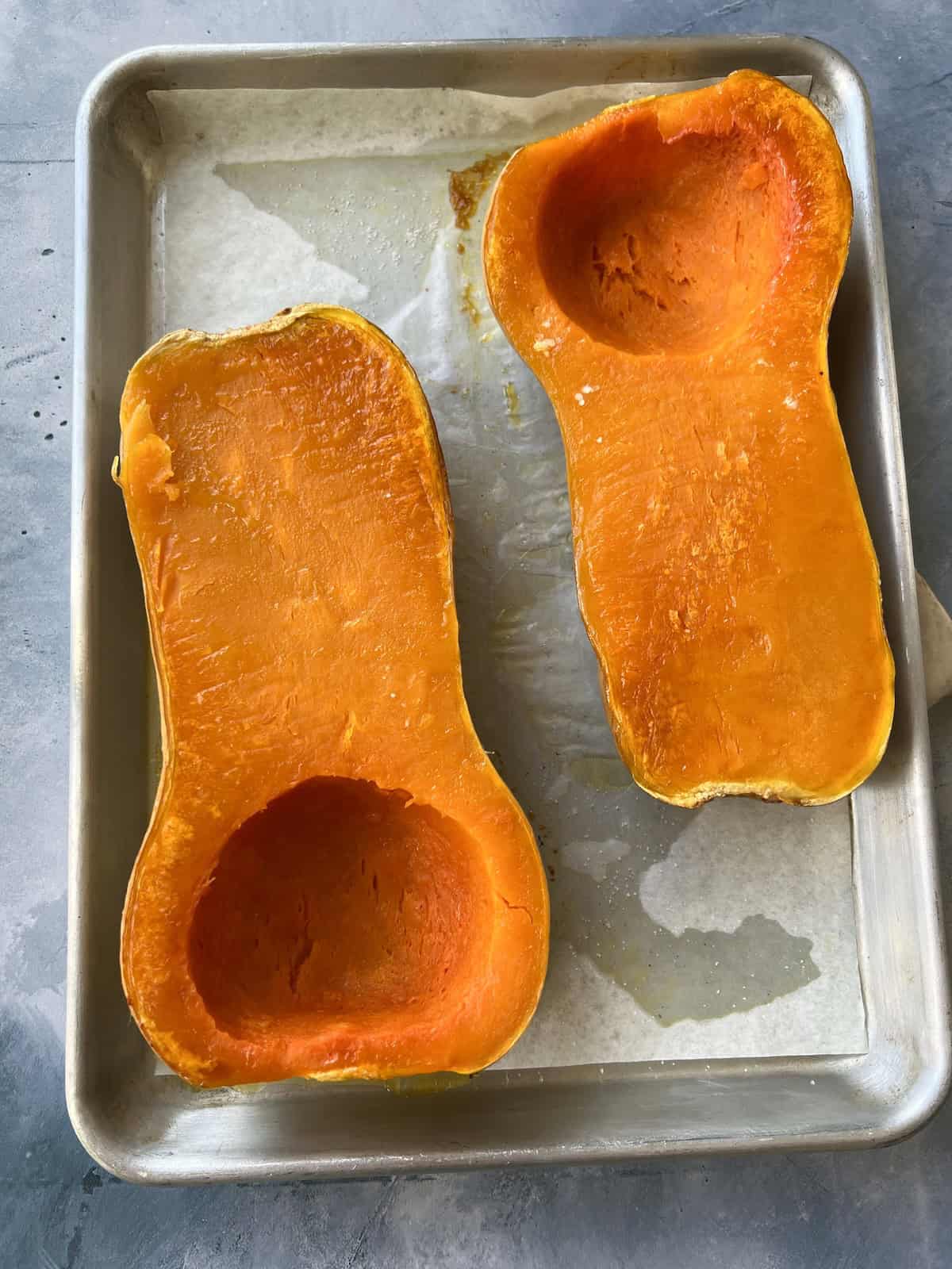 the roasted butternut squash halves have a deep orange coloring and soft, slightly collapsed appearance. 