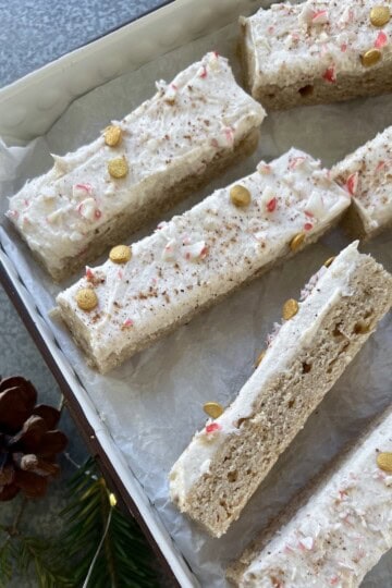 eggnog cookie bars are sprinkled with crushed candy cane and gold sprinkles, then arranged up in a parchment paper lined serving tray