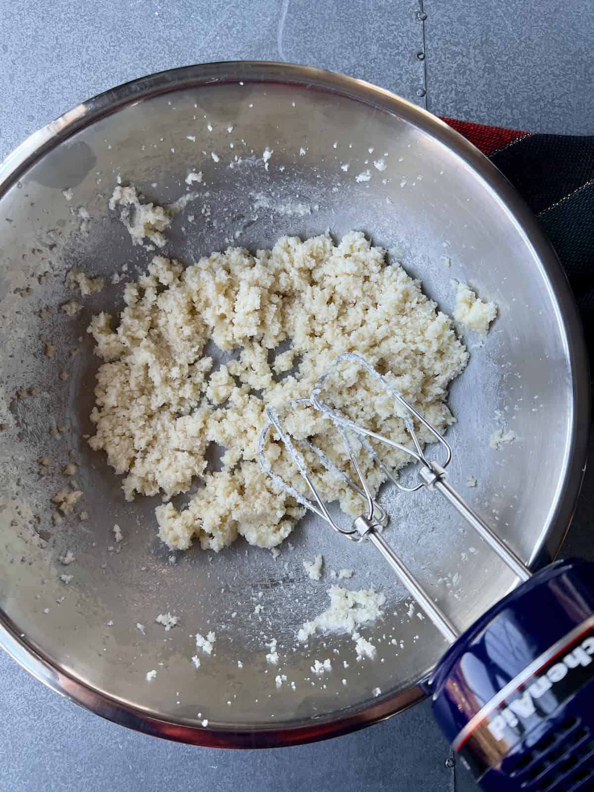 whipped butter and sugar in a mixing bowl with a handheld mixer leaning in