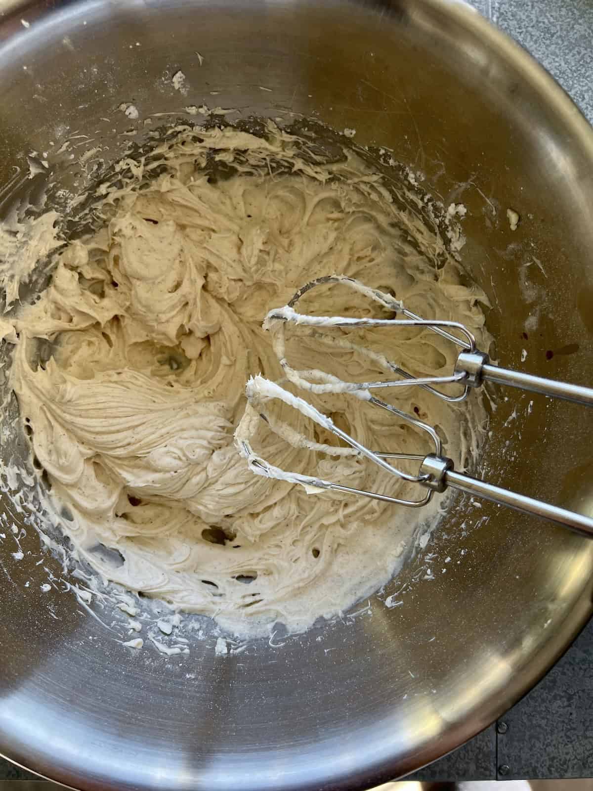 a bowl of fully whipped eggnog frosting with the beaters of a handheld mixer leaning in