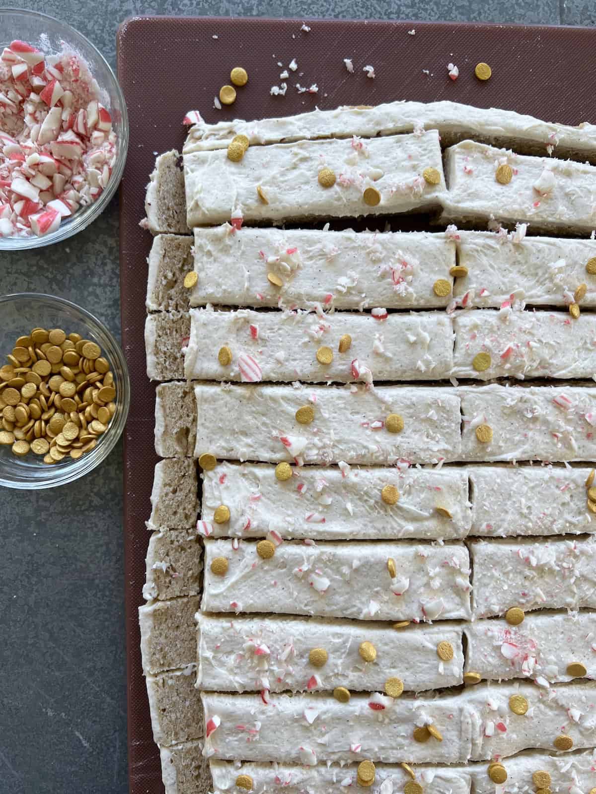the frosted eggnog cookie bars are topped with a sprinkling of crushed candy cane and small round gold sprinkles