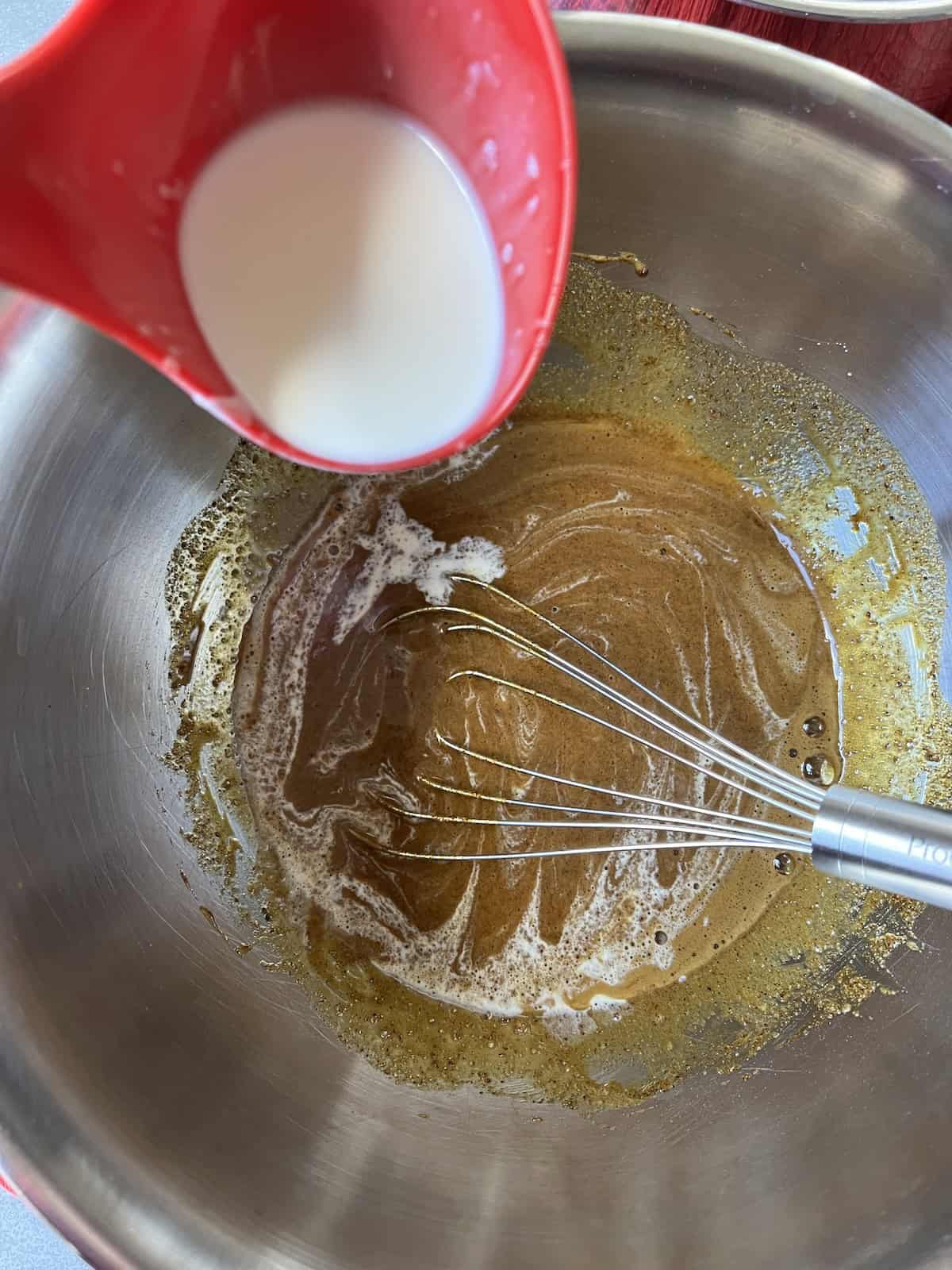 a ladleful of heavy cream is held over the bowl of egg yolk mixture