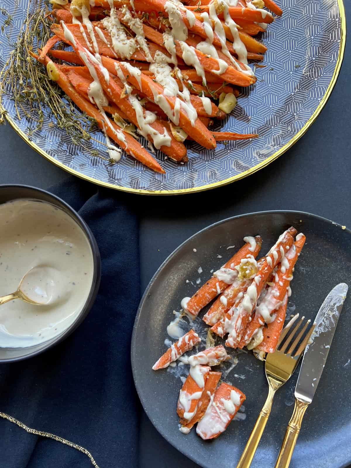 a portion of roasted carrots with tahini sauce are moved to a plate, then sliced and eaten with a knife and fork