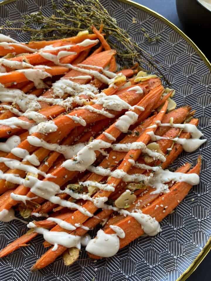 tahini sauce is drizzled over roasted carrots in a diagonal pattern, then garnished with toasted sesame seeds