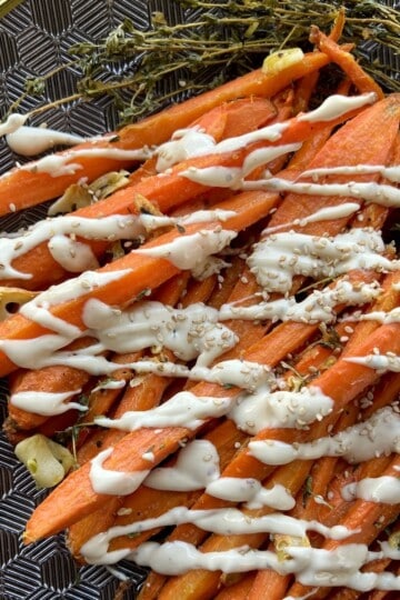 long strips of roasted carrots are lined up on a serving platter and drizzled with tahini sauce