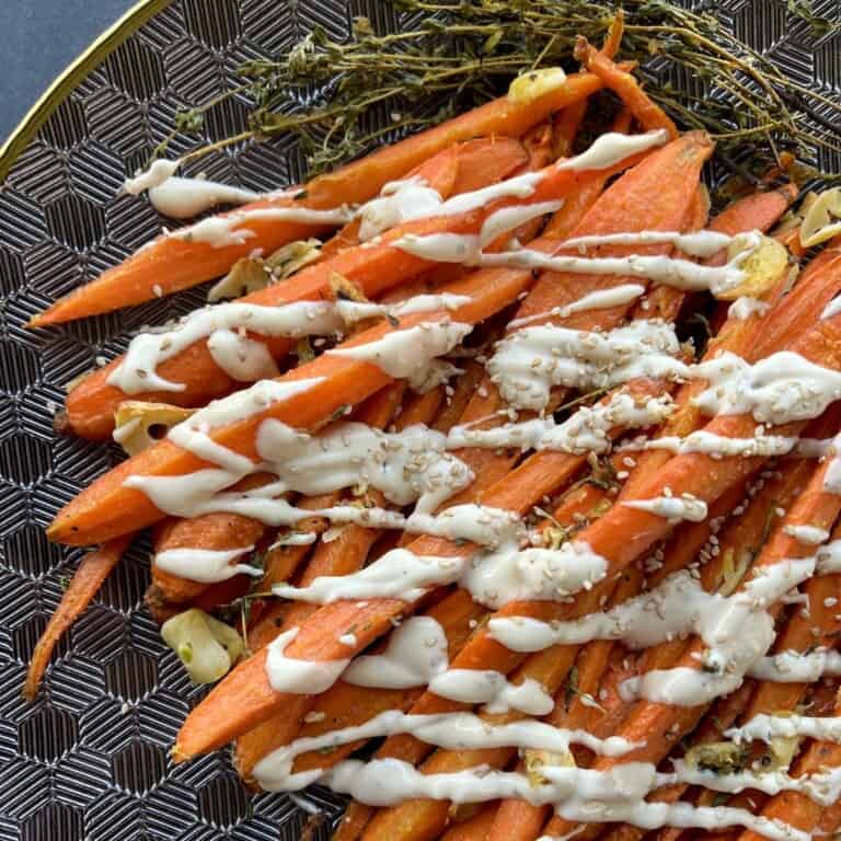 long strips of roasted carrots are lined up on a serving platter and drizzled with tahini sauce