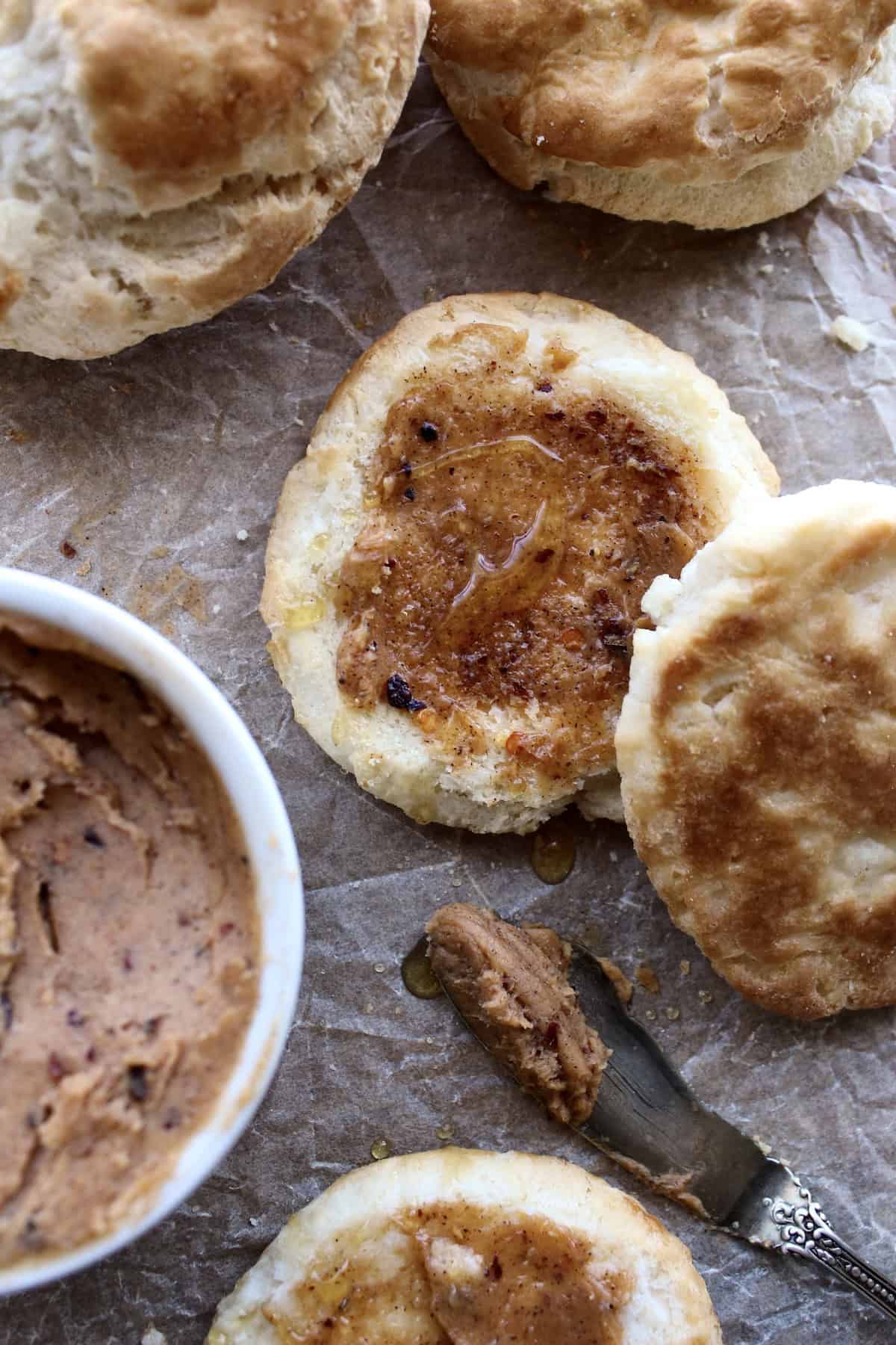 hot honey butter is spread on a halved biscuit using an antique silver spreader