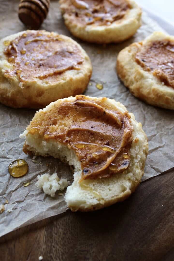 a wooden board with warm halved biscuits, each one smeared with thick hot honey butter and drizzled with extra honey