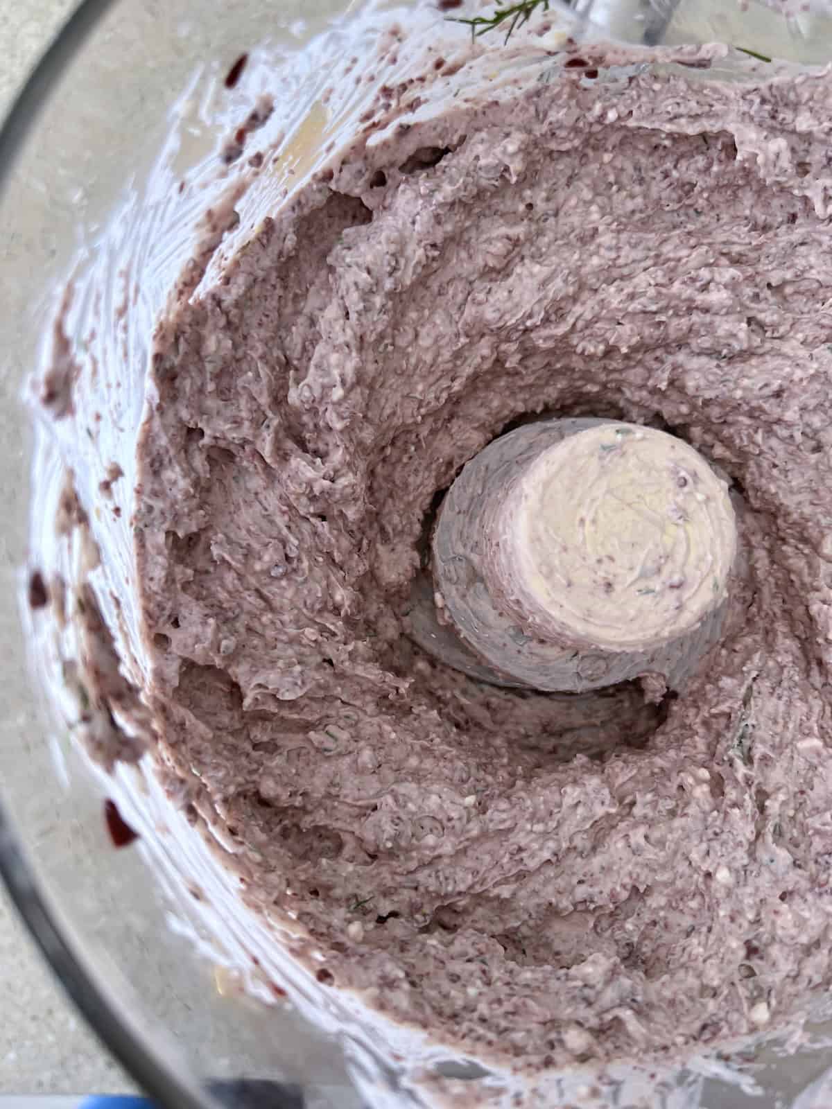 the ingredients are processed into a thick puree, with visible pieces of olive, dill, and feta cheese.