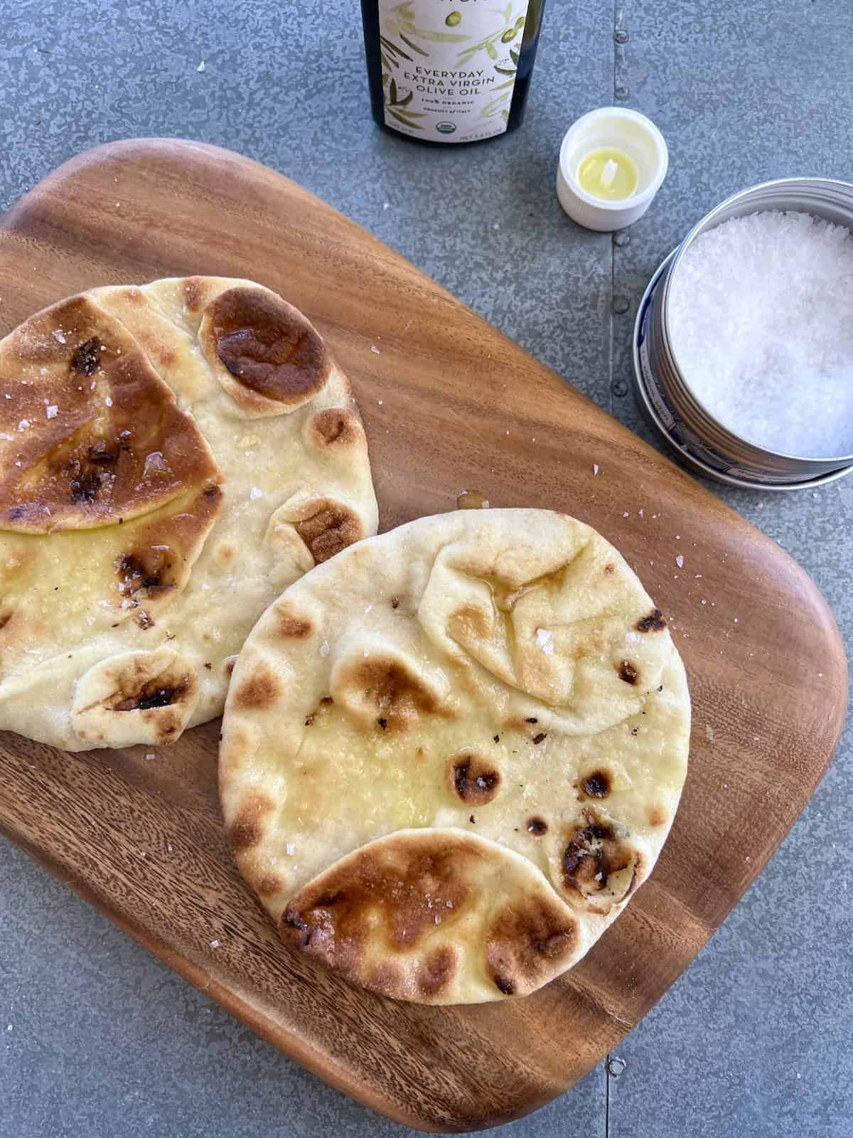 rounds of pita bread are set on a cutting board and drizzled with olive oil