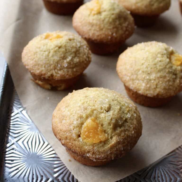 baked orange muffins are arranged on a decorative parchment paper lined baking sheet