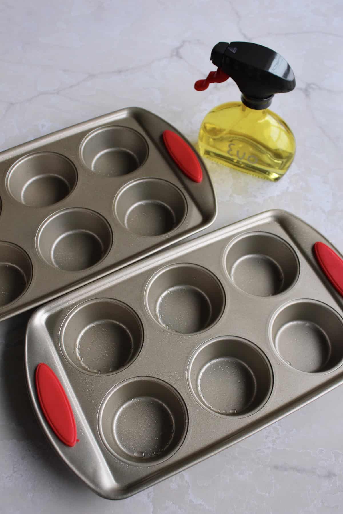 two 6-hole muffin tins sitting next to an oil sprayer