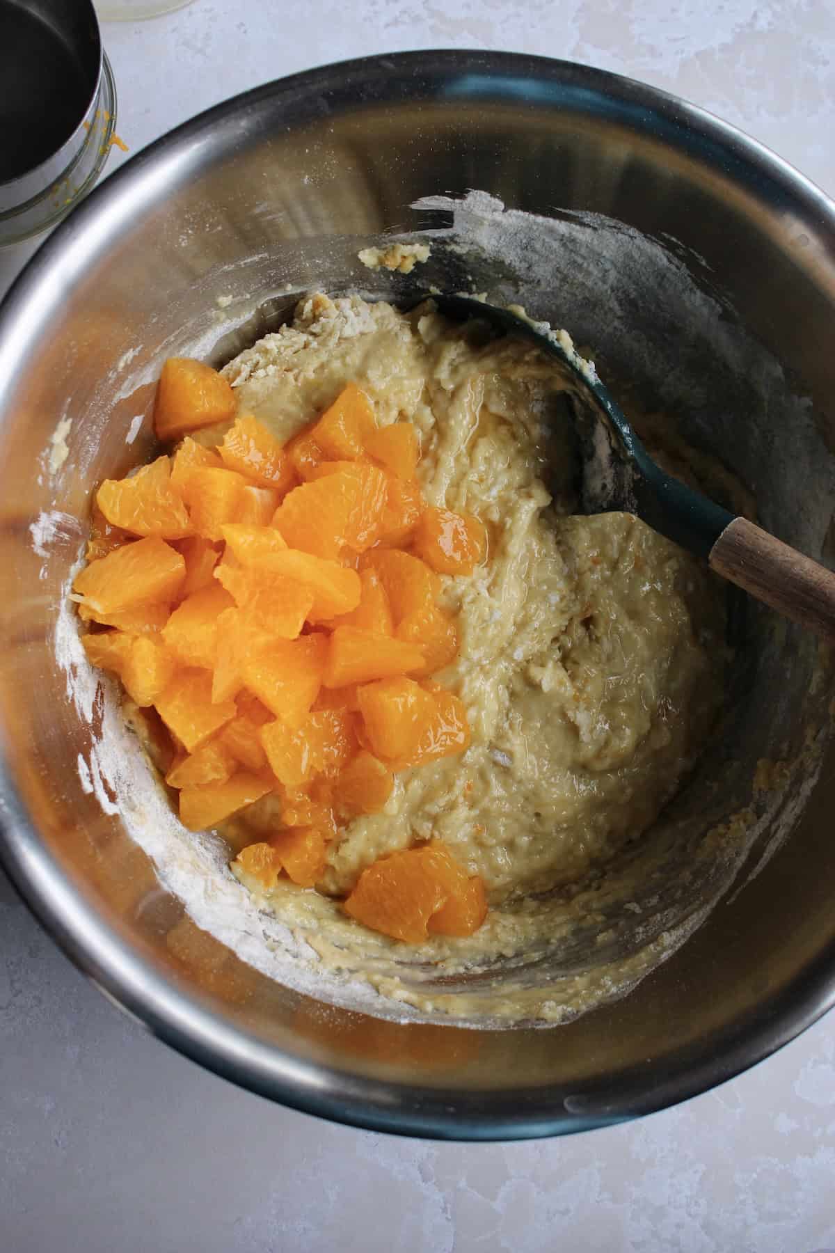 chopped orange segments are added to the bowl of partially mixed muffin batter