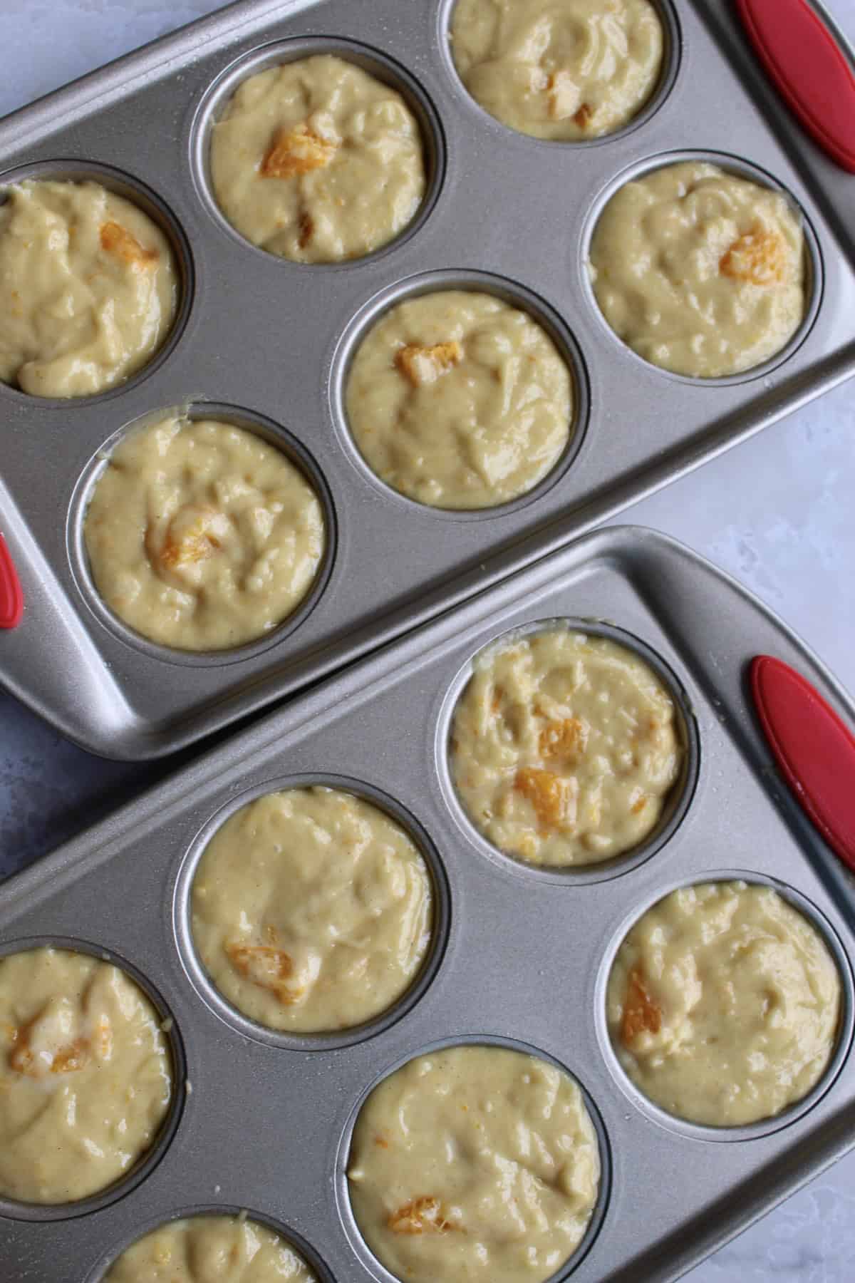 two 6-hole muffin pans are filled with the orange muffin batter